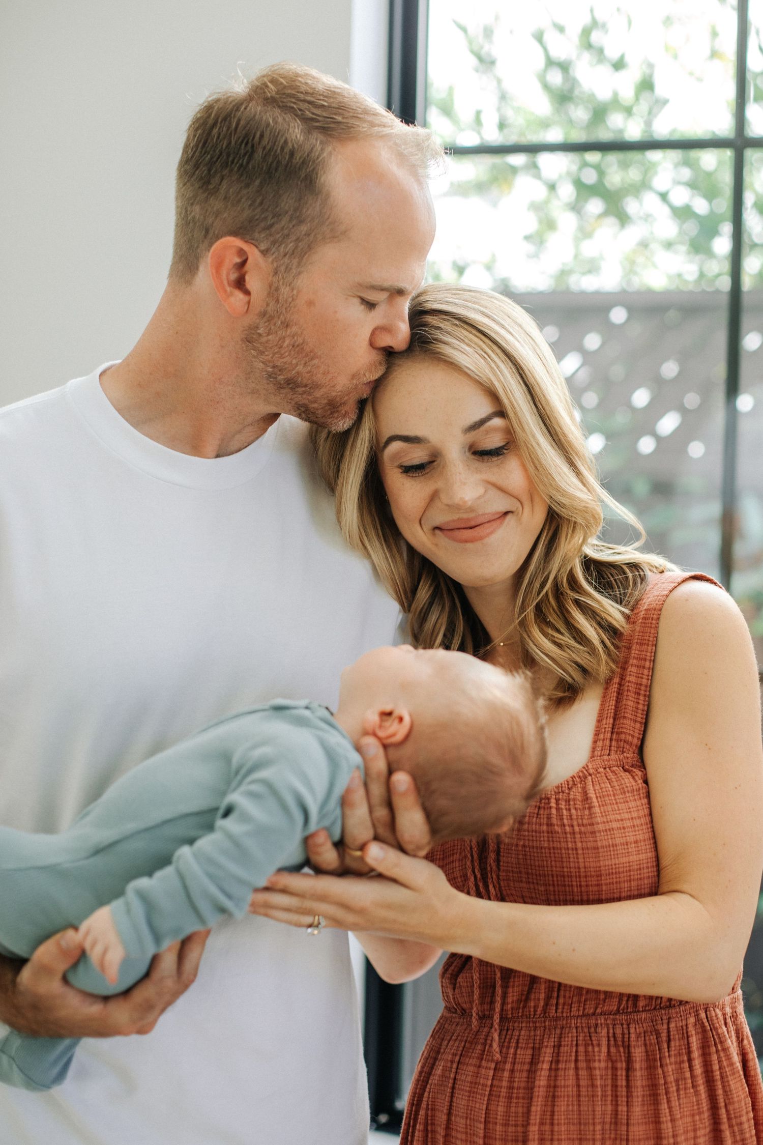 Loving father kissing mother's head as they both admire their newborn baby together.