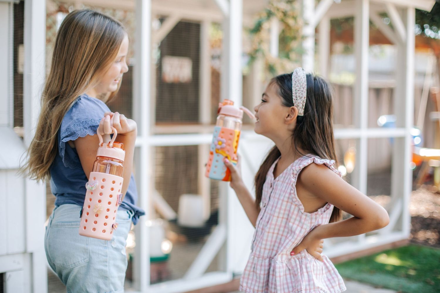Two young girls outdoors holding colorful spotted glass water bottles with silicone sleeves.