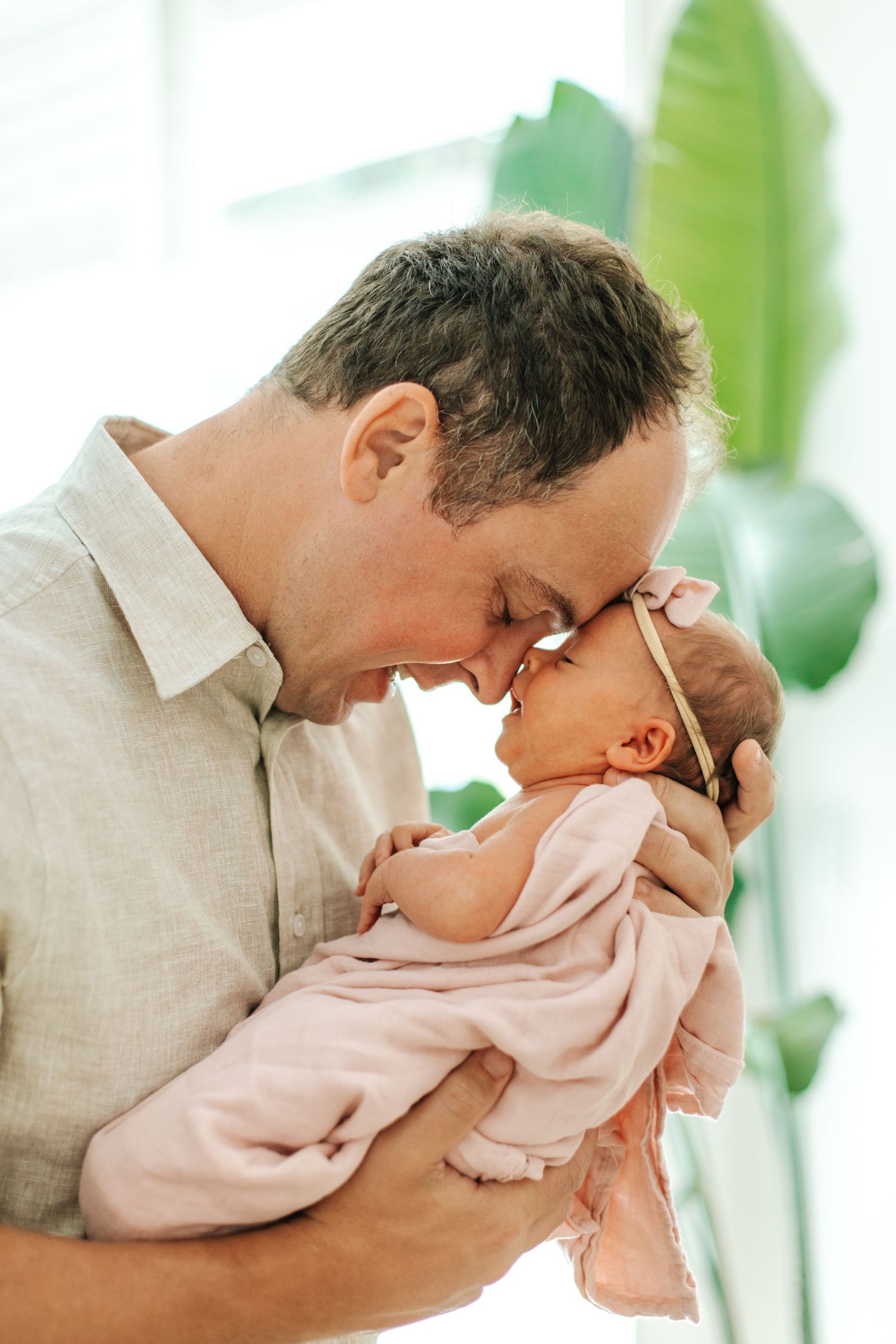 Tender moment as a father touches foreheads with his newborn baby girl wrapped in pink.