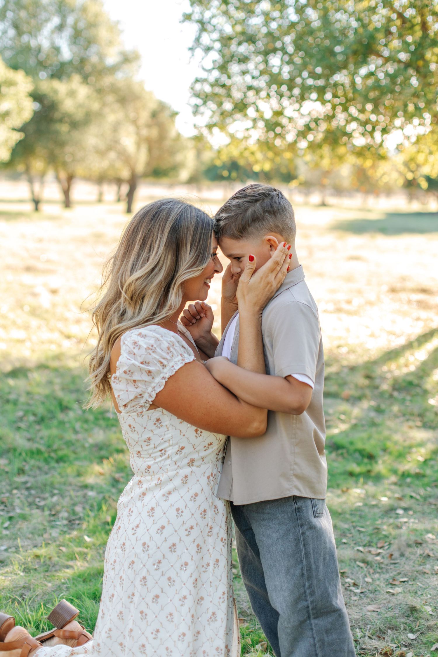 Romantic couple embracing forehead-to-forehead in a sunlit park, woman in white floral dress.