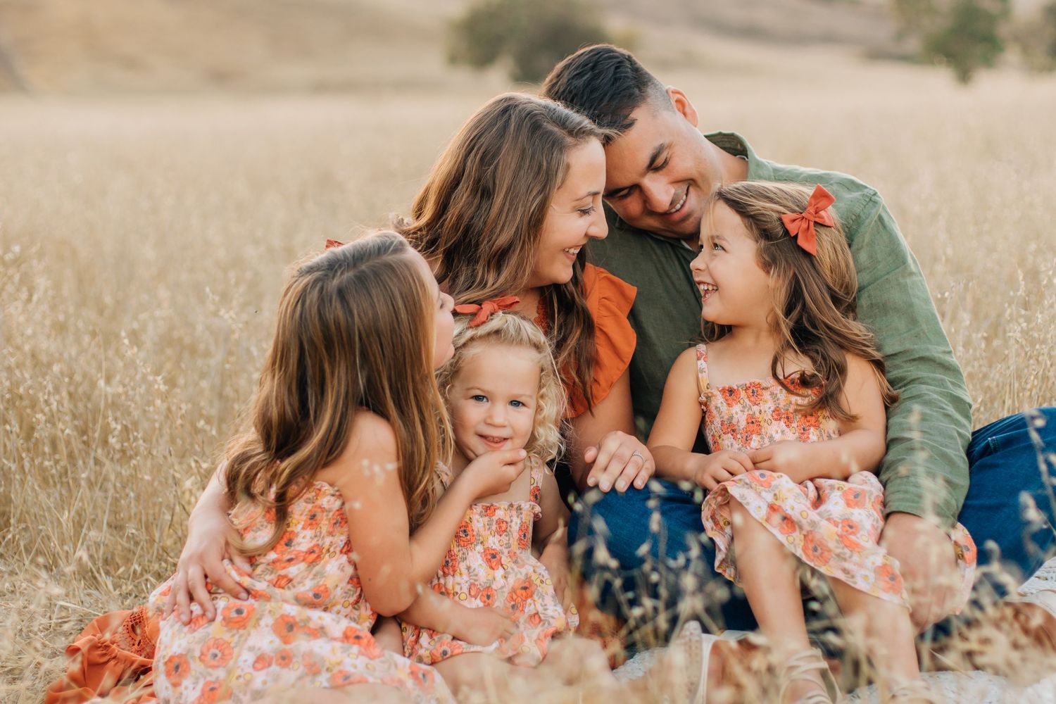 Happy family of five sitting together laughing in a golden wheat field.