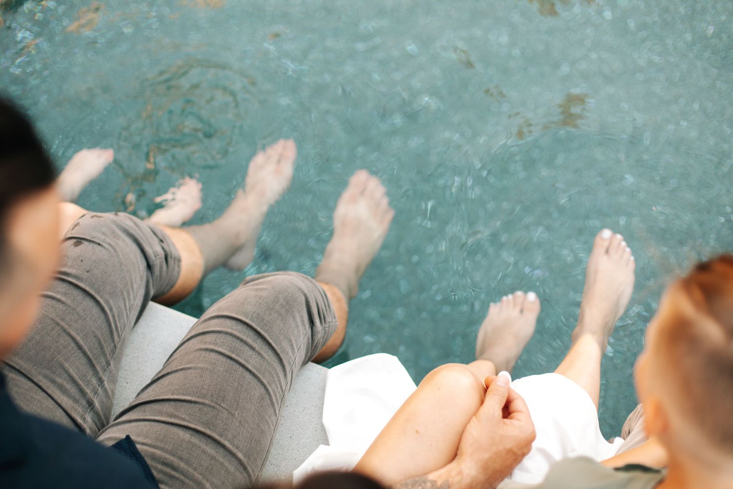 A close-up overhead view of four people sitting poolside with bare feet dipping into the water.