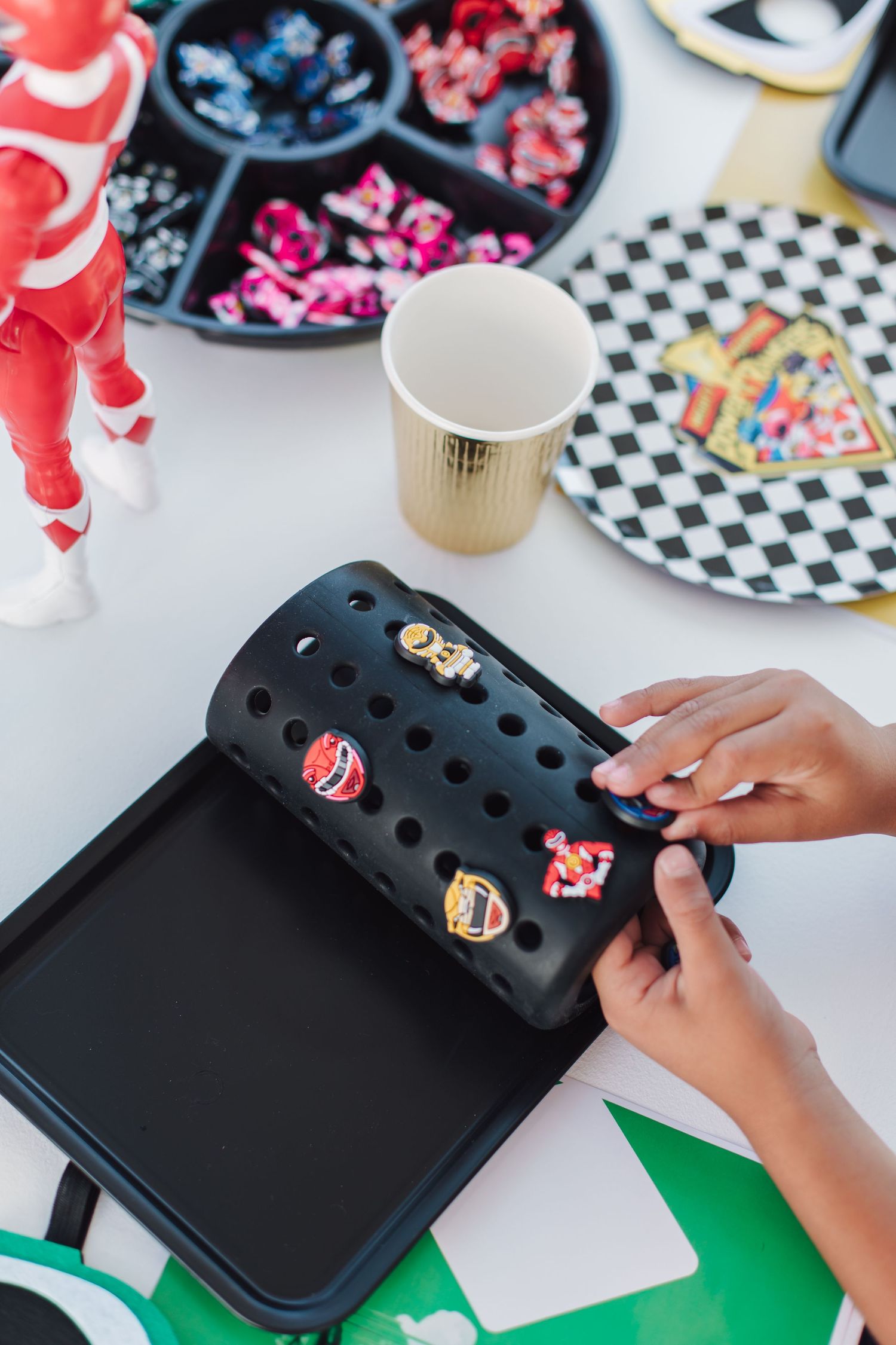 Child decorating black Croc shoe with Power Rangers Jibbitz charms at themed birthday party.