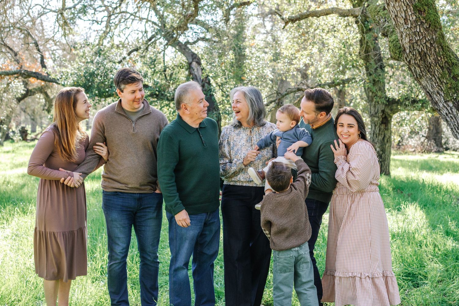 Extended multigenerational family laughing and gathering together in a sunlit green meadow.