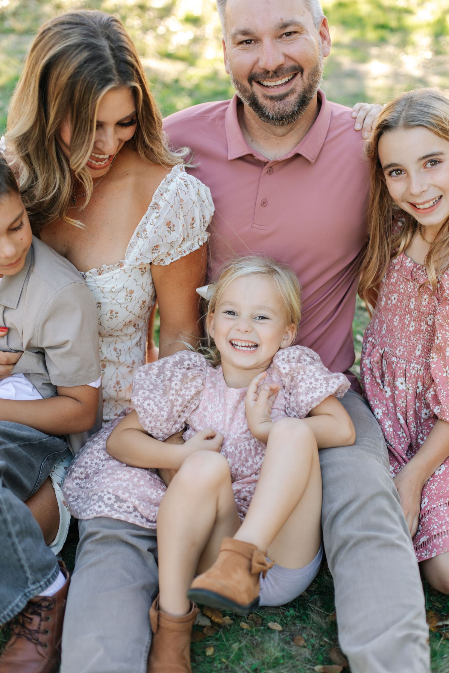 Smiling family of five sitting outdoors, parents with three children posing for portrait in park.