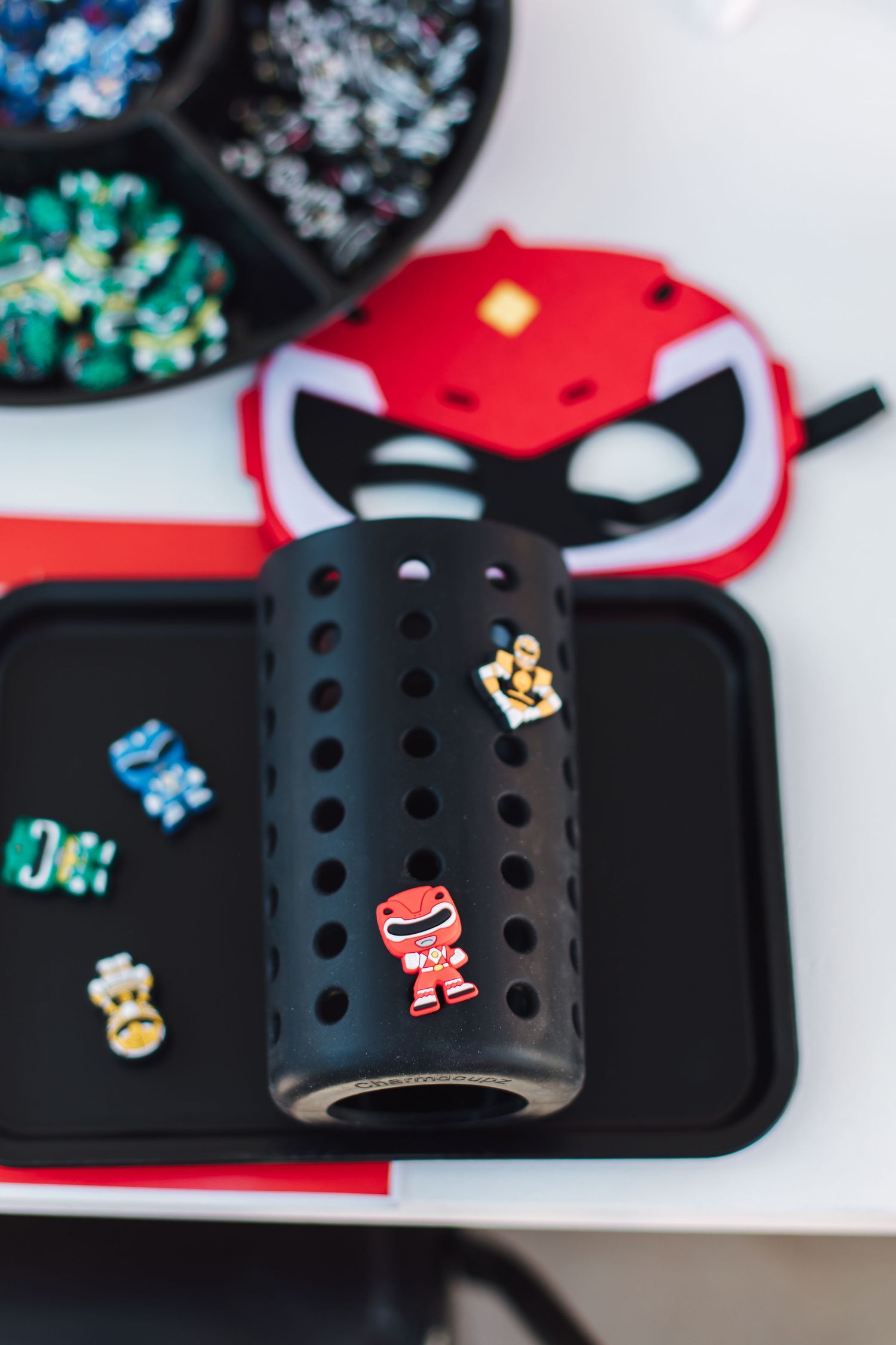 Power Rangers themed party activity with black Croc shoe and colorful Jibbitz charms on tray.