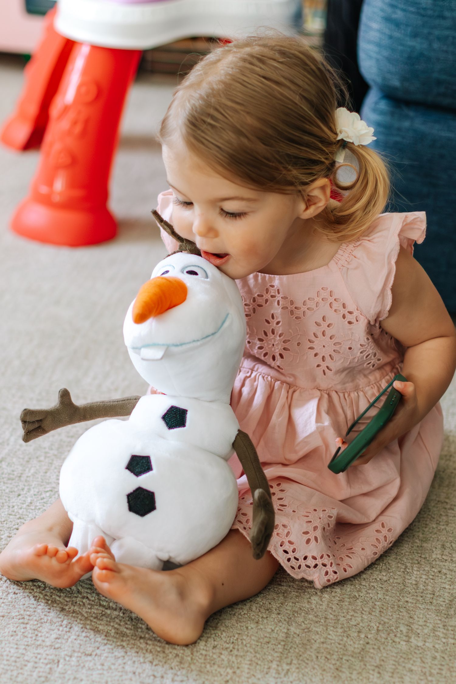 A toddler girl in a pink dress hugs an Olaf snowman plush toy.