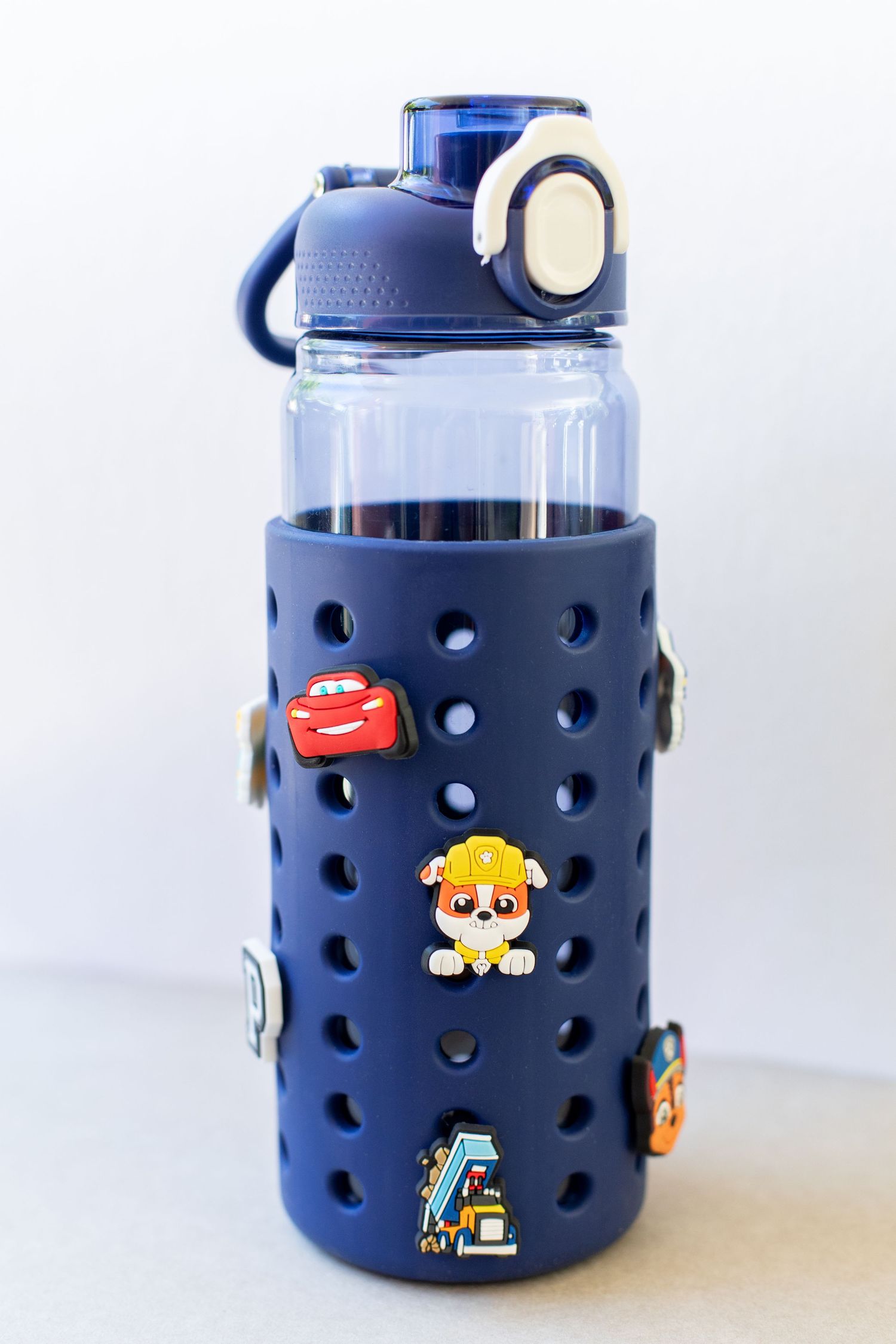 Navy blue silicone sleeve water bottle decorated with Paw Patrol character charms on white background.