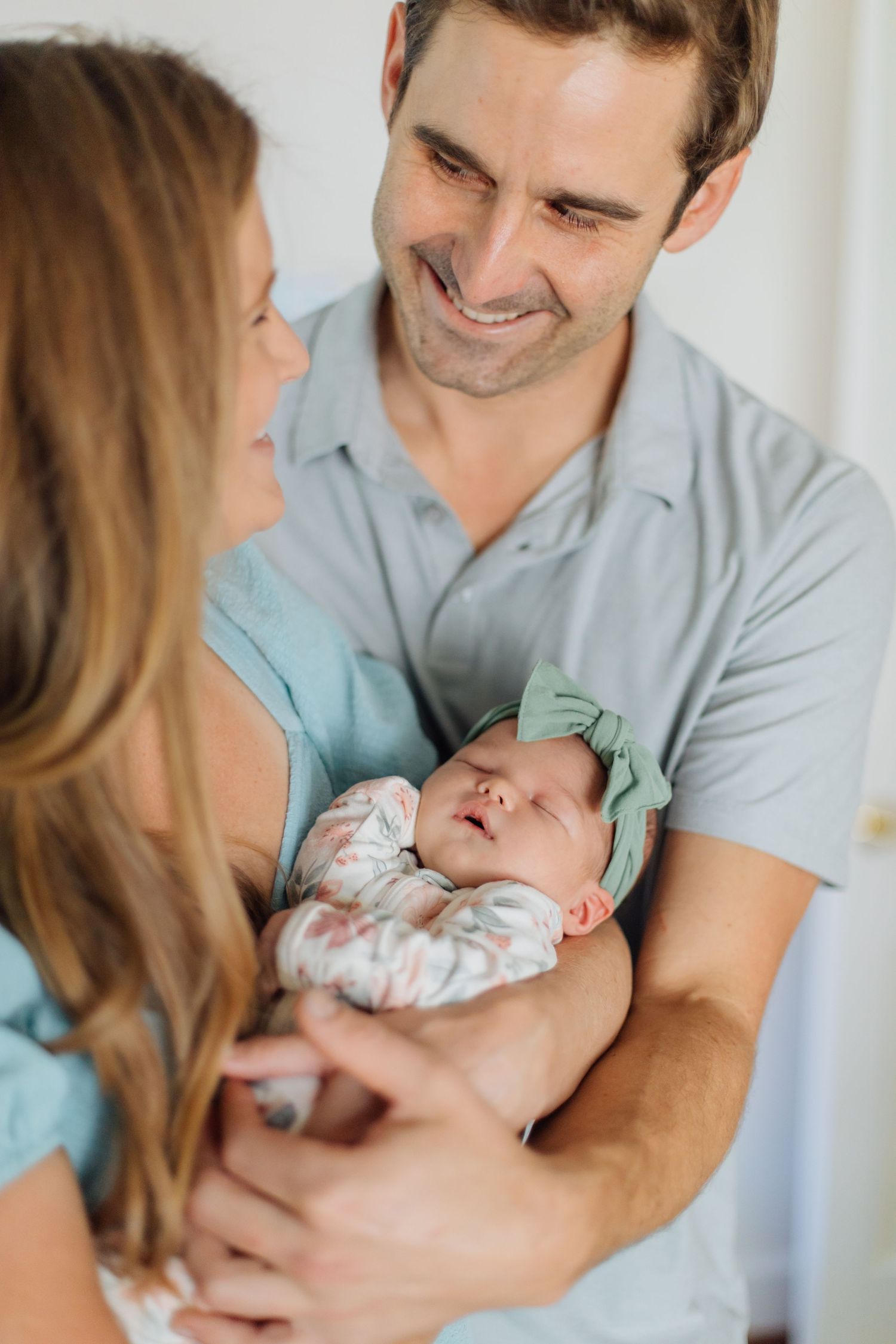 Smiling new parents gazing at their sleeping newborn baby girl wrapped in a floral blanket.