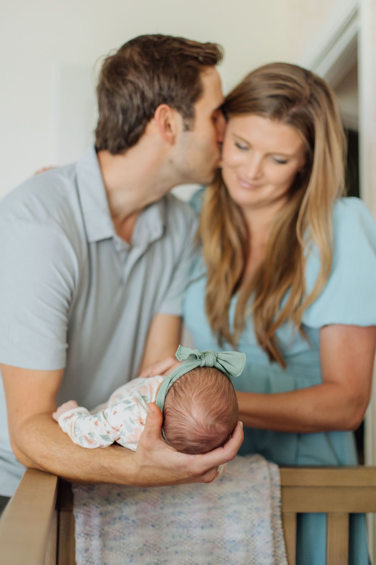 New parents lovingly holding their newborn baby girl as father kisses mothers cheek.