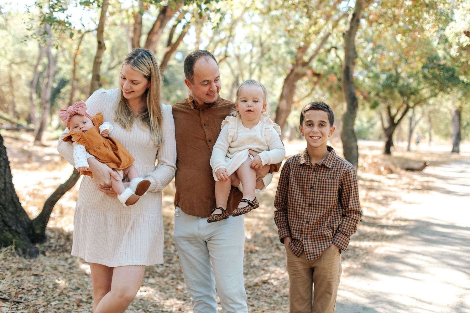 A blended family of five walks along a tree-lined path in warm autumn light.