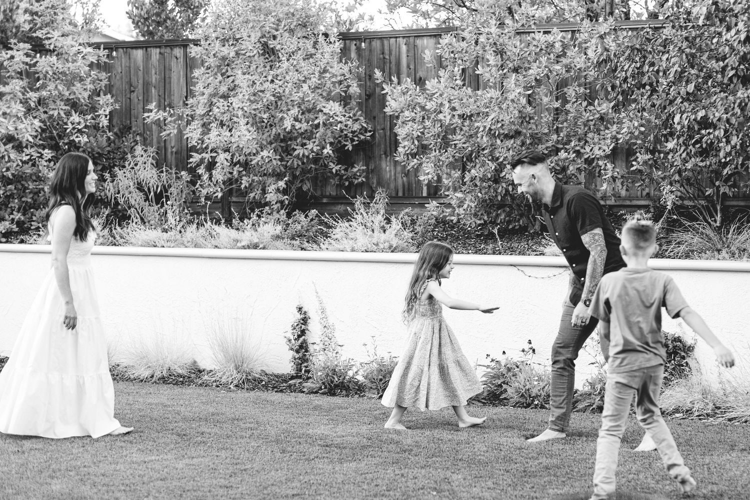 A black and white photo of a family playing together on a lush landscaped backyard lawn.