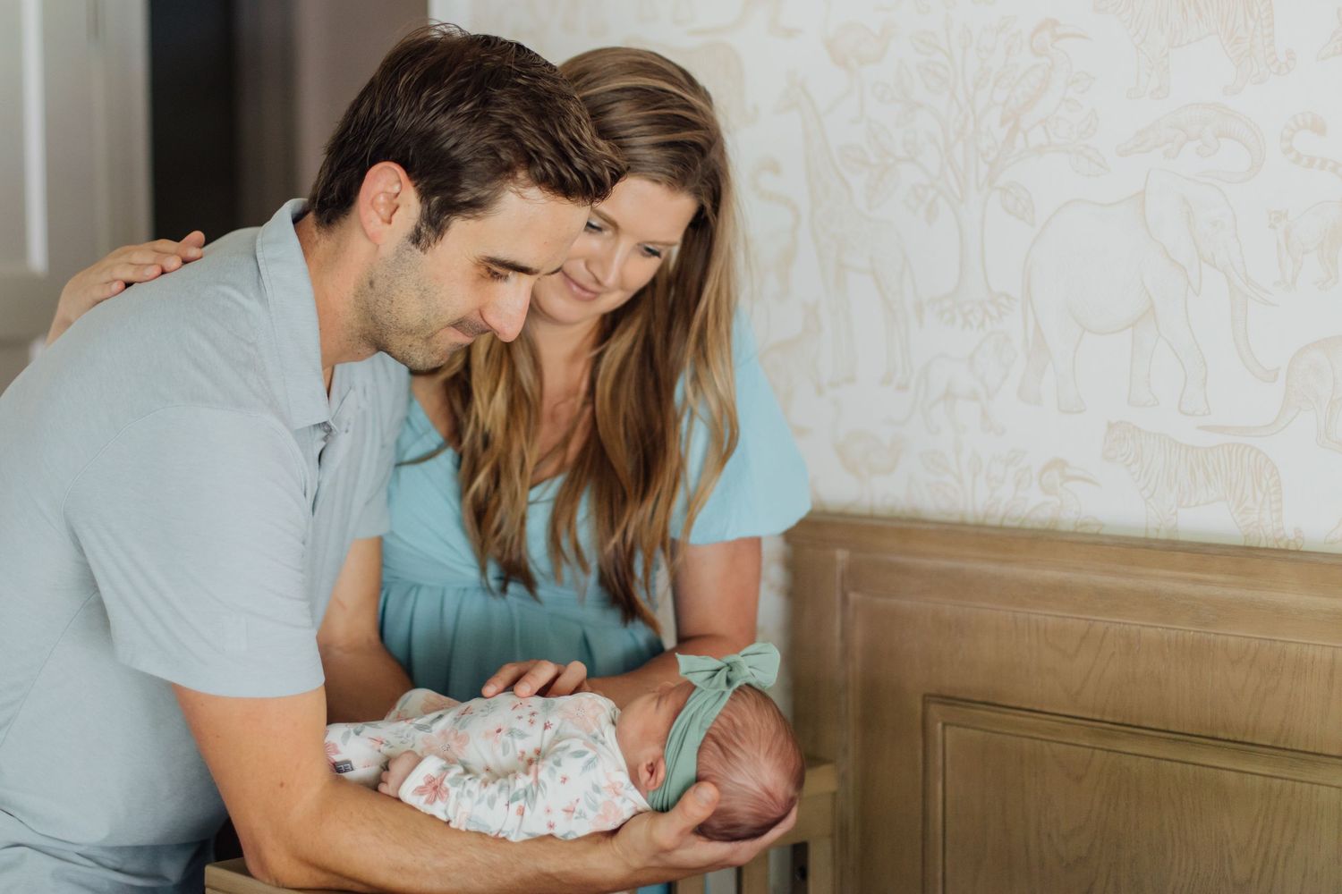 A couple in matching blue outfits lovingly gazes at their newborn baby in a nursery.