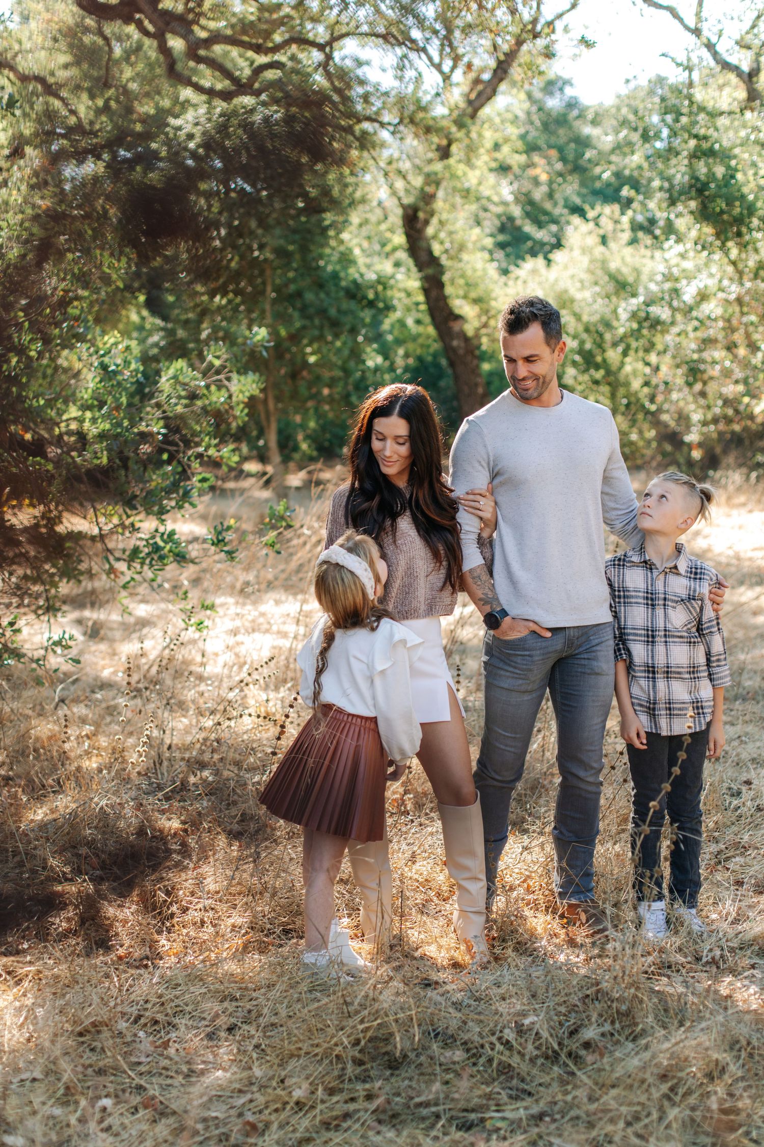 Family of four standing together in a sun-drenched meadow surrounded by trees.