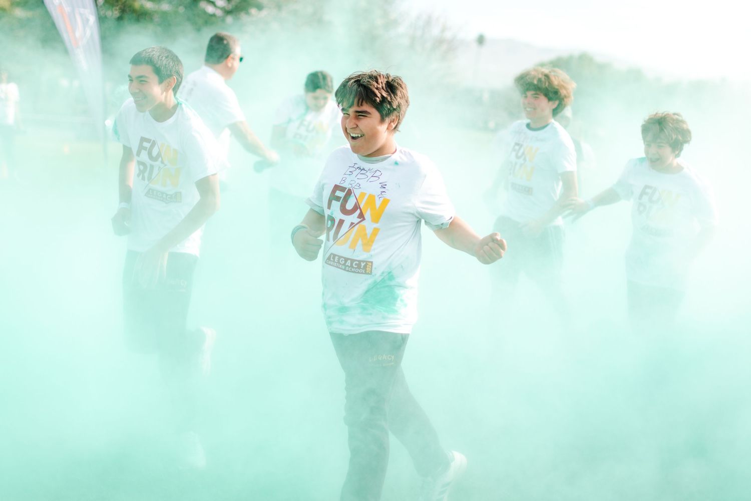 Children running through colorful green powder cloud during fun run charity event outdoors.