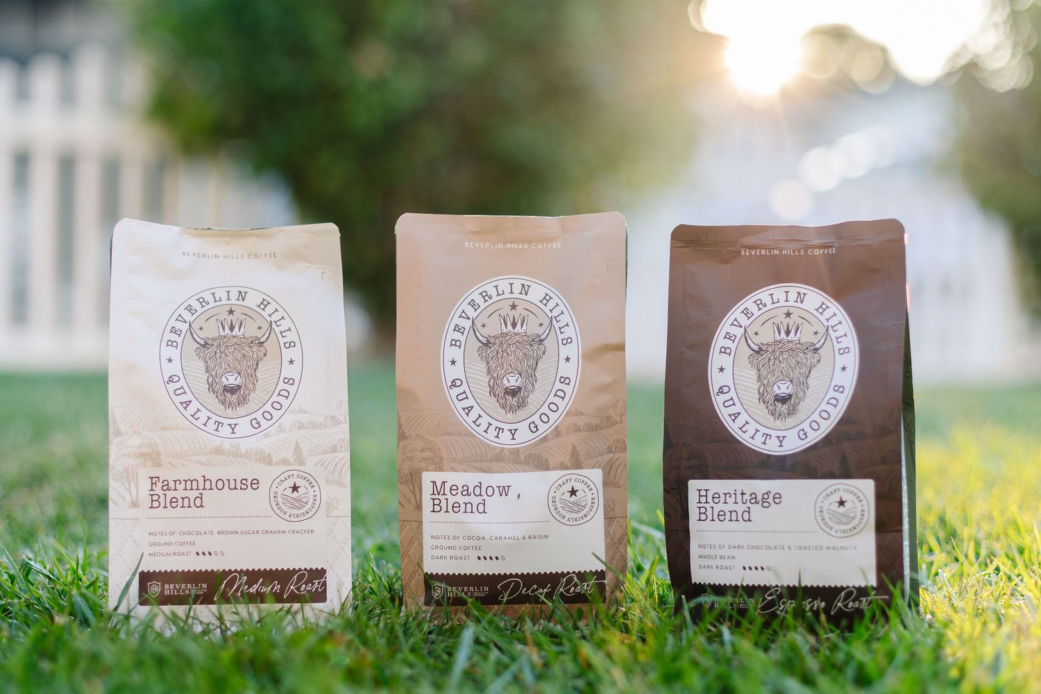 Three bags of Beverlin Hills Quality Goods coffee blends displayed on green grass in sunlight.