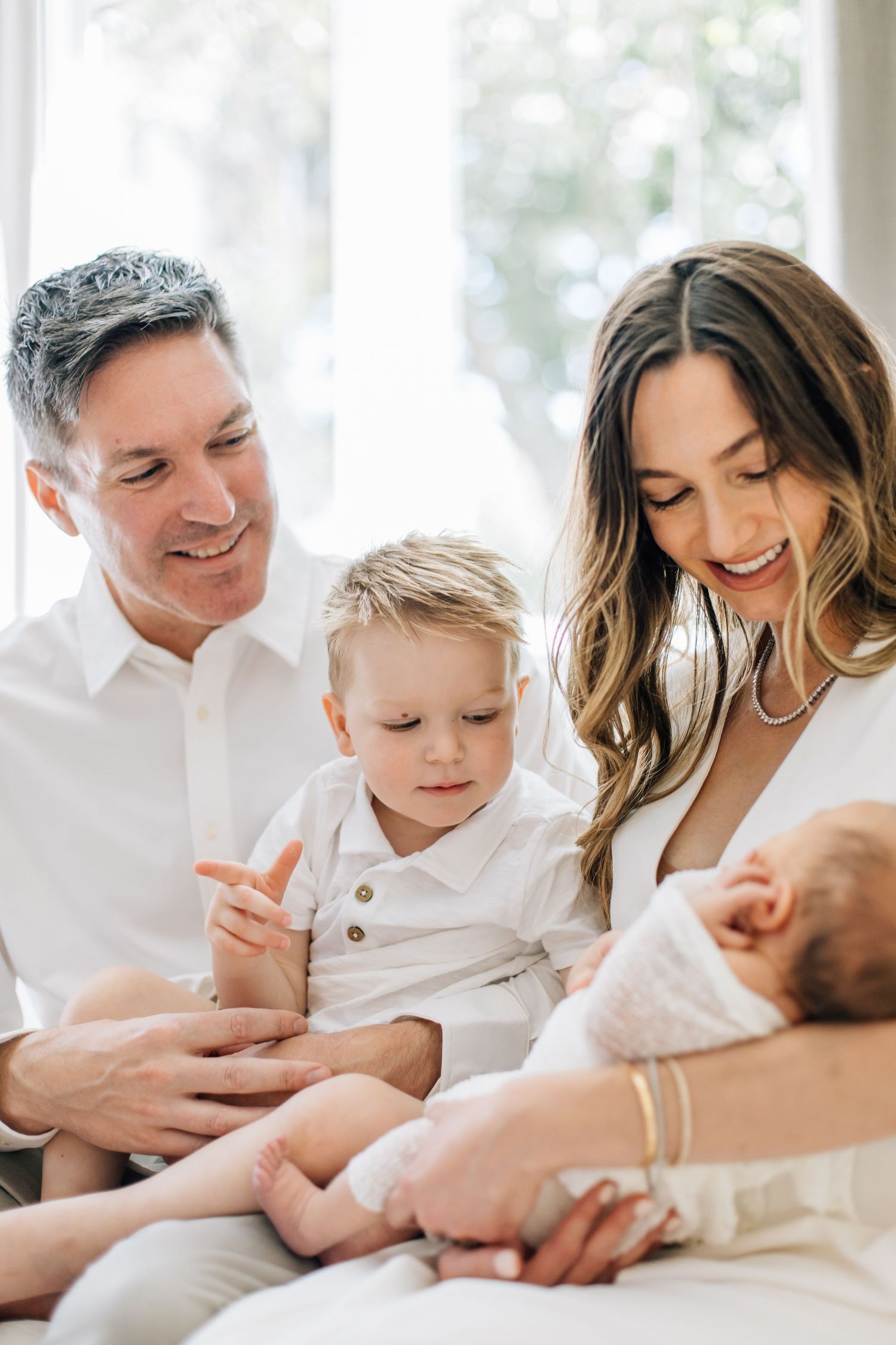 Smiling family of four with parents and two young children admiring their newborn baby.