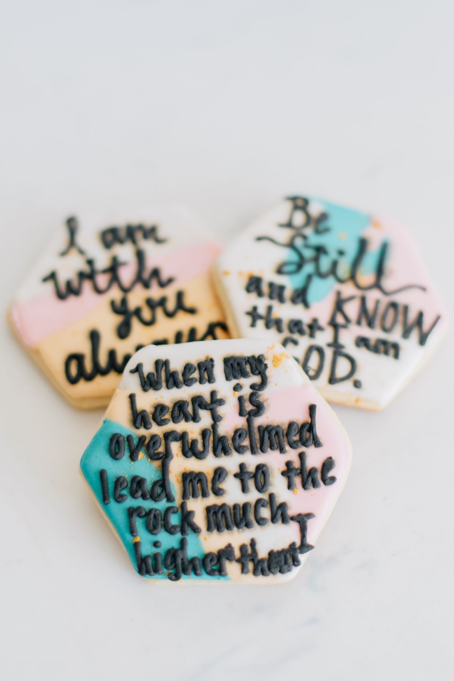 Three hexagonal frosted sugar cookies with hand-lettered Bible verse scripture quotes in black icing.
