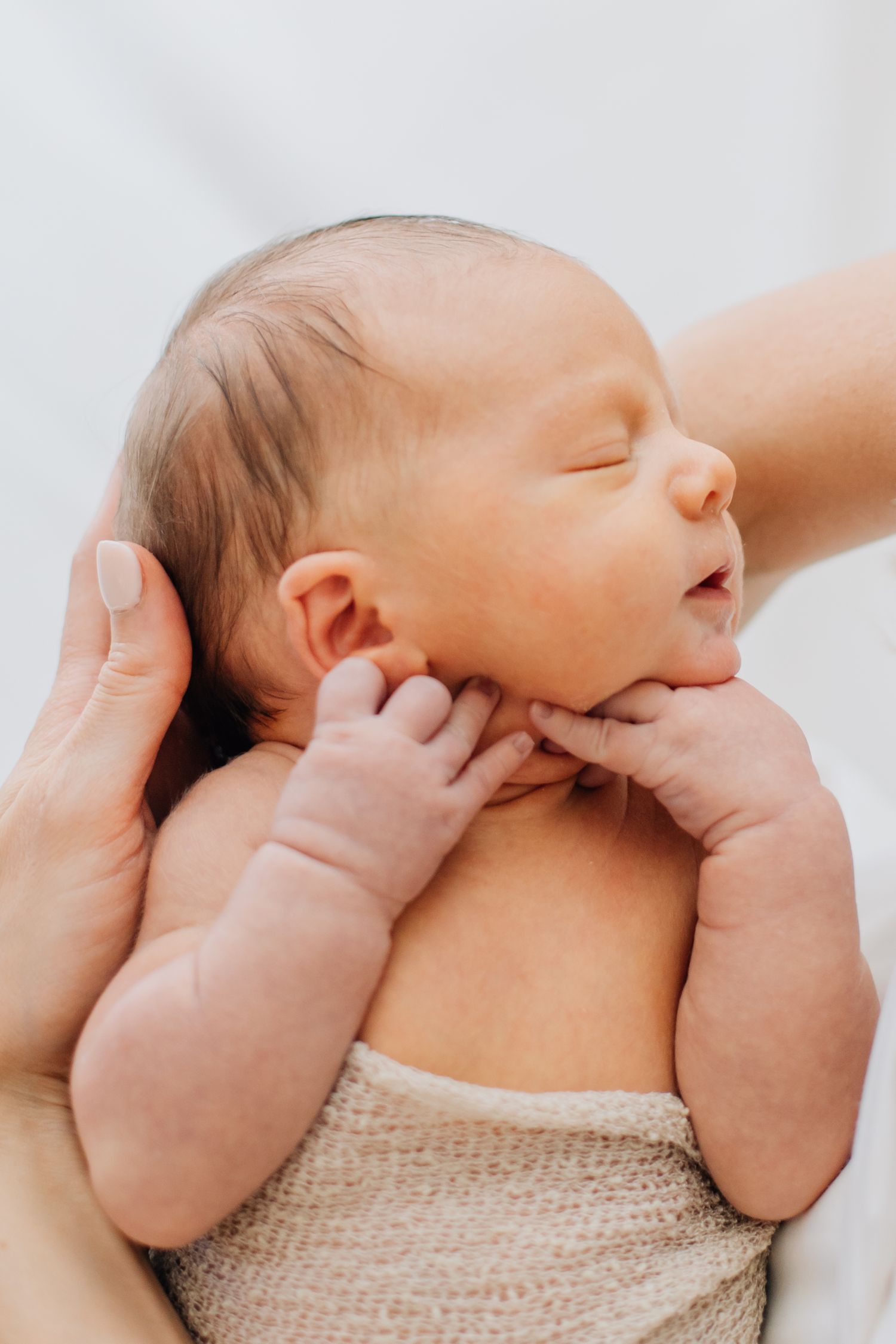 Close-up of peaceful sleeping newborn baby held gently in parent hands wrapped in beige knit.