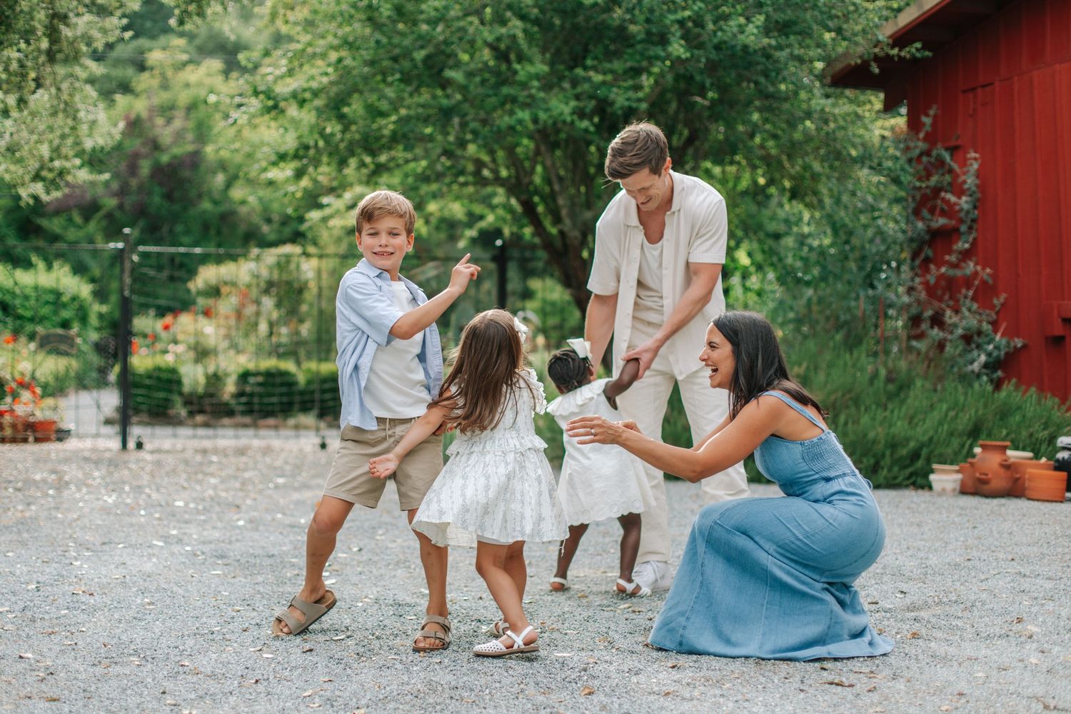 Family gathered together playing and laughing on a gravel path near a charming red barn.
