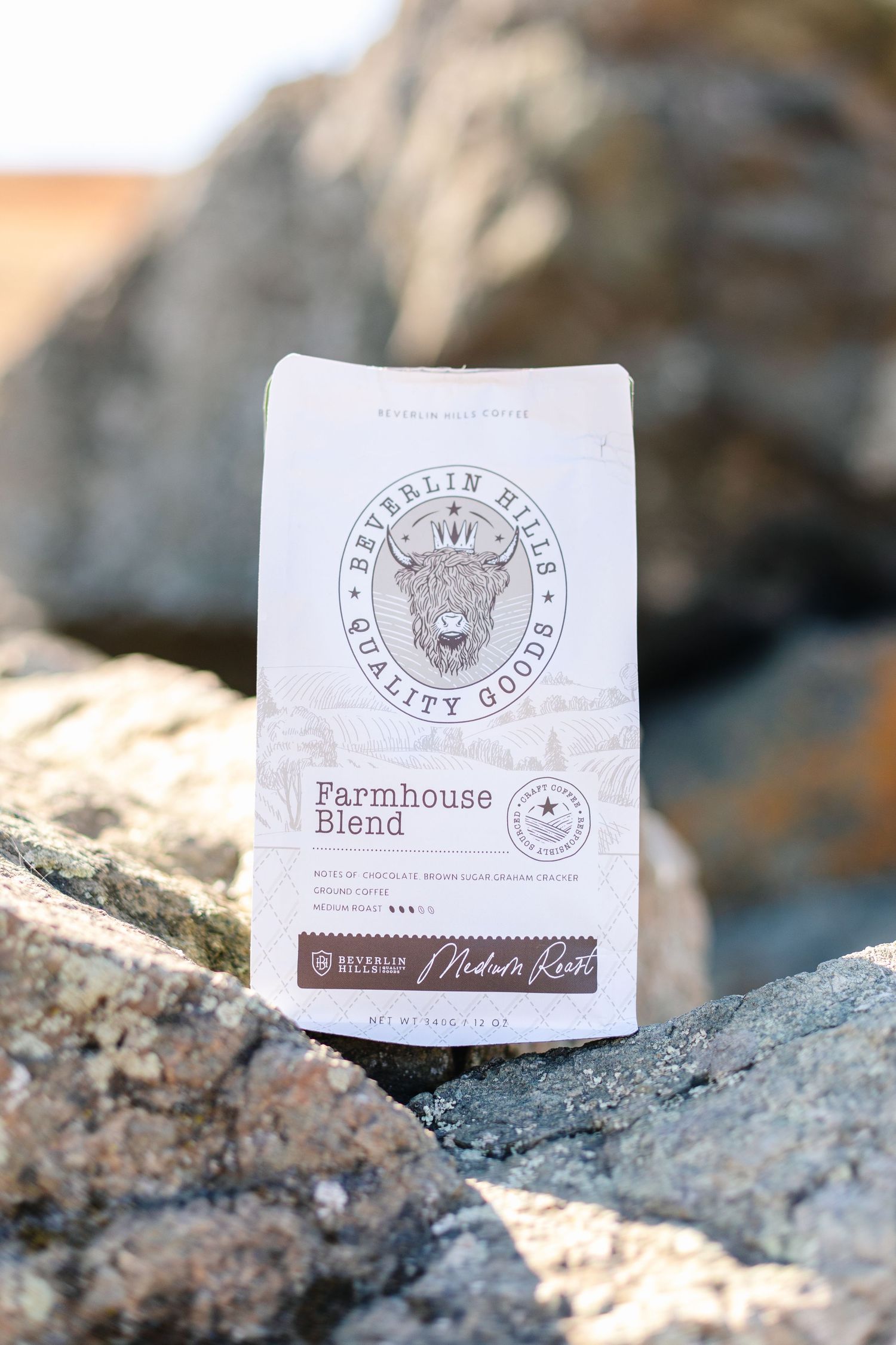 Beverlin Hills Quality Goods Farmhouse Blend medium roast coffee bag displayed on rocks outdoors.