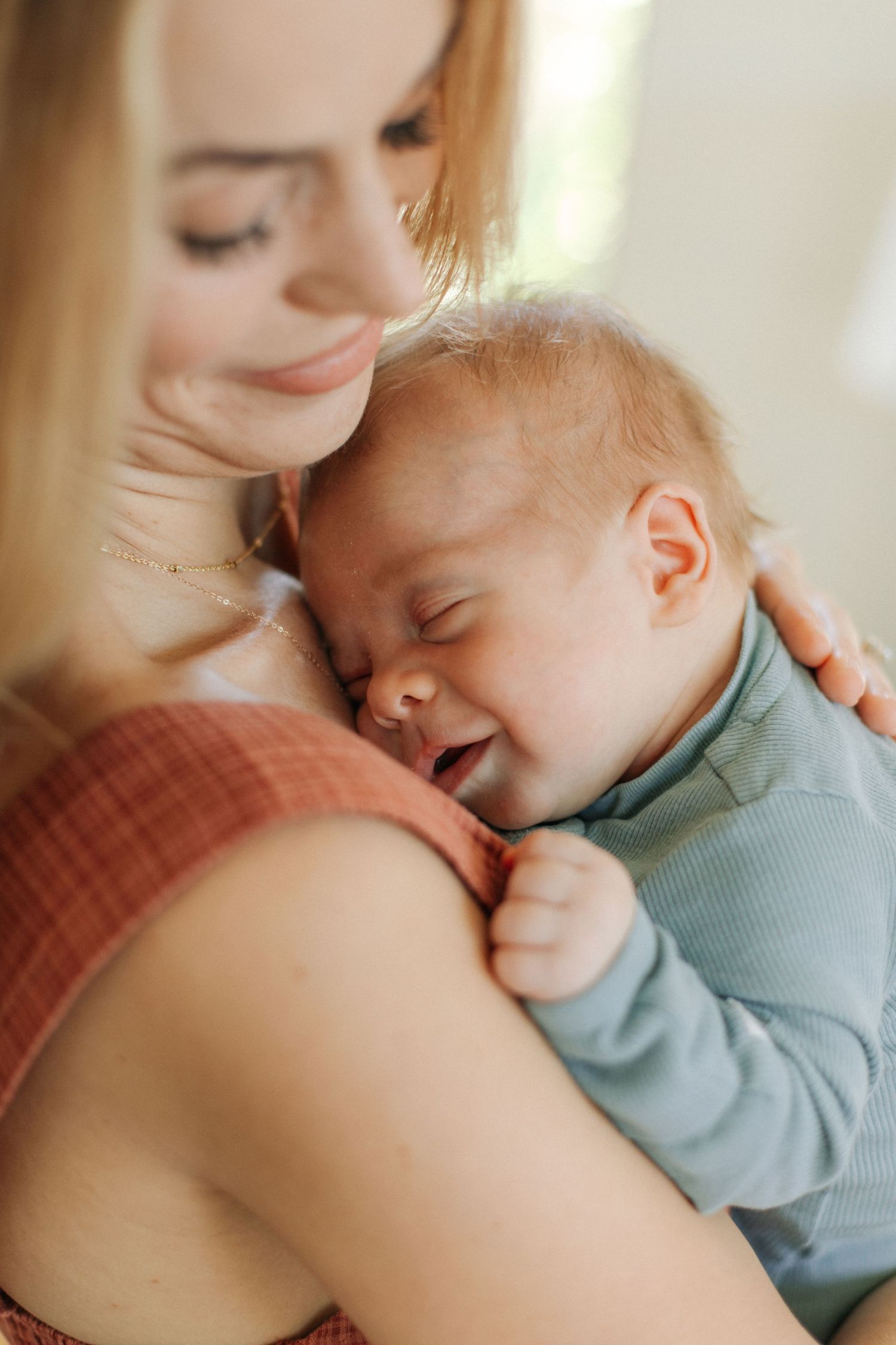 Smiling mother tenderly holding her sleeping newborn baby dressed in a light blue onesie.