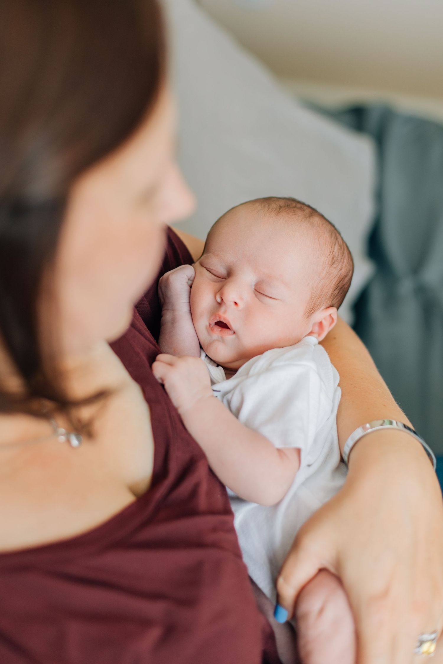 Sleeping newborn baby in white onesie resting peacefully in mothers arms at home.