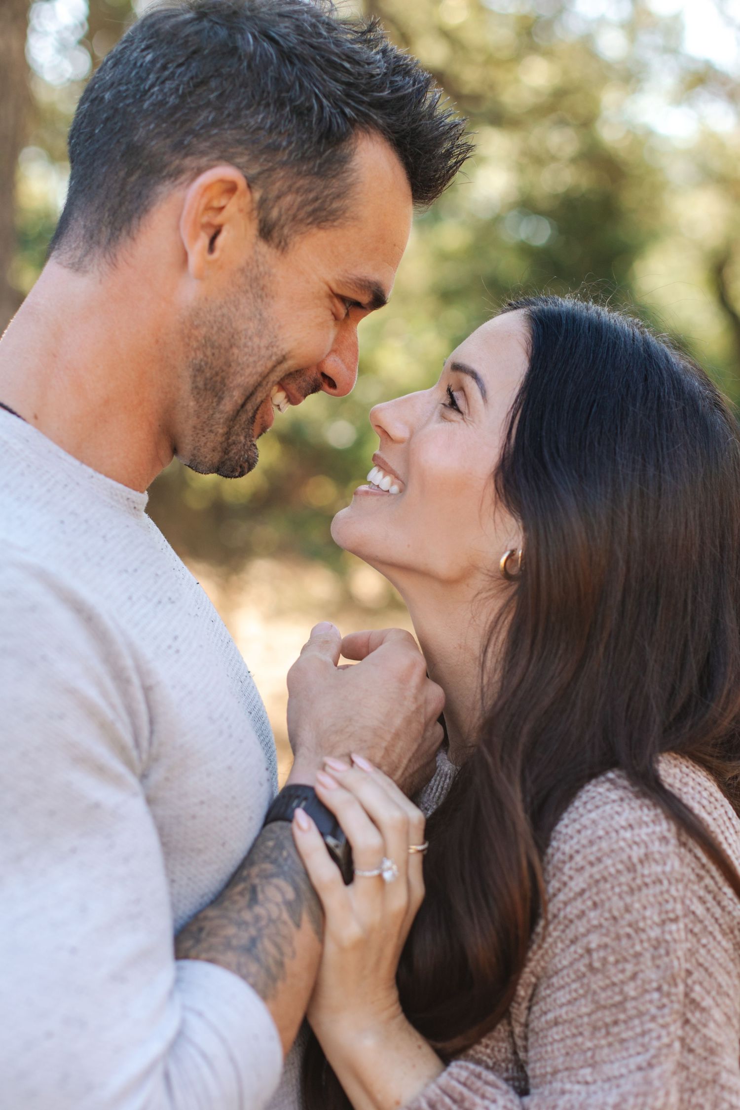 Romantic couple smiling face to face while holding hands in a sunny park.