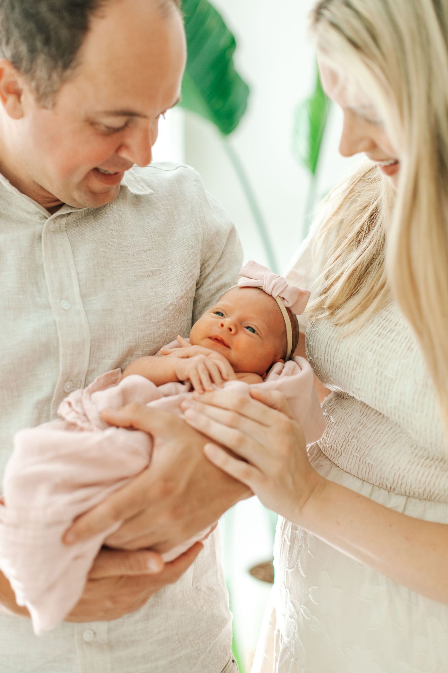 Loving parents gaze down at their newborn baby girl wrapped in a soft pink blanket.
