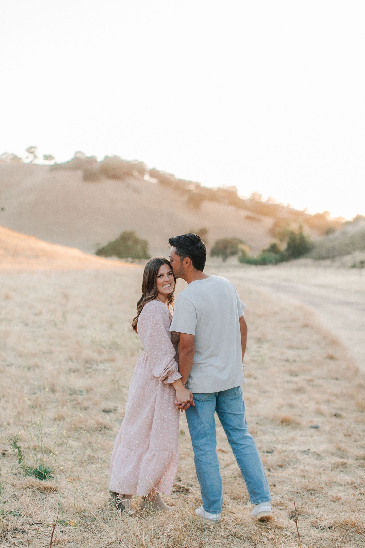 Romantic couple holding hands and sharing a quiet moment in a golden sunlit open field.