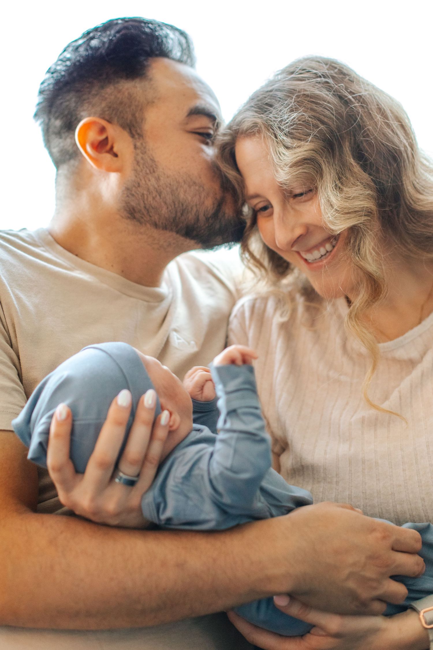 Happy couple kissing and smiling while holding their newborn baby wrapped in a blue blanket.
