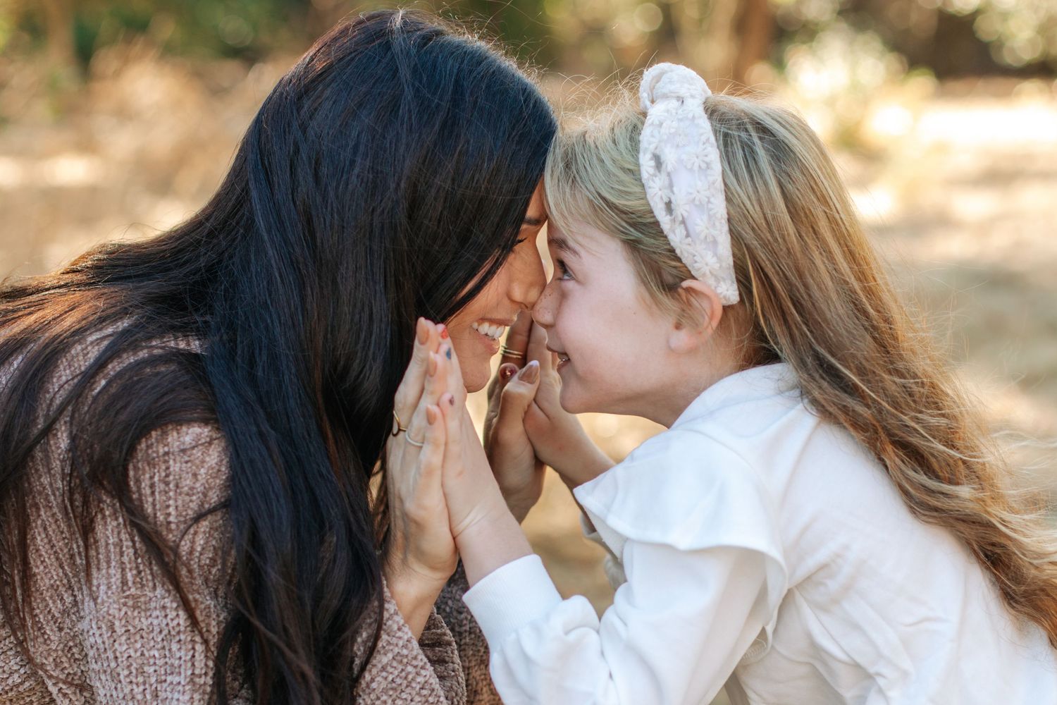 Mother and young daughter sharing a tender nose-to-nose moment outdoors in soft natural light.