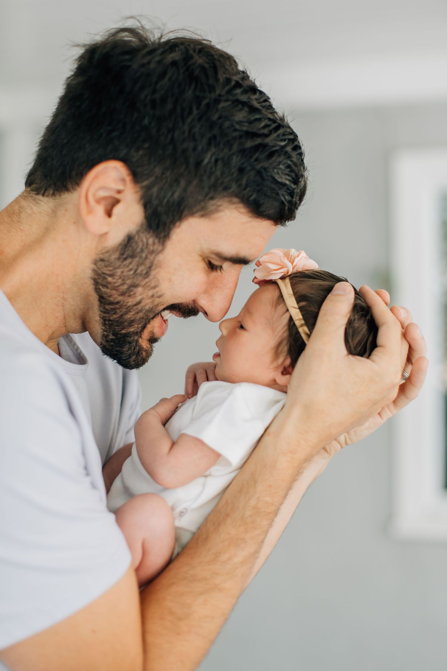 Loving father gently touches foreheads with his newborn baby girl wearing a bow headband.