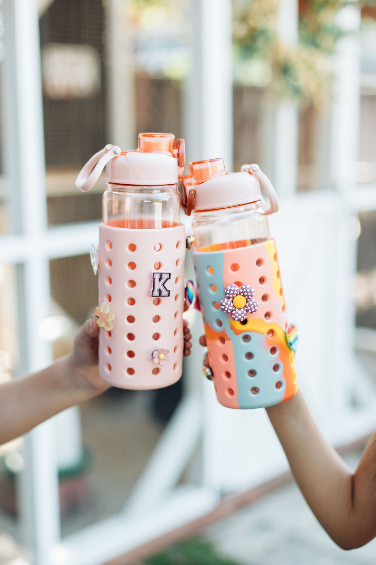 Two colorful silicone-sleeved glass water bottles with fun stickers being clinked together in a toast.
