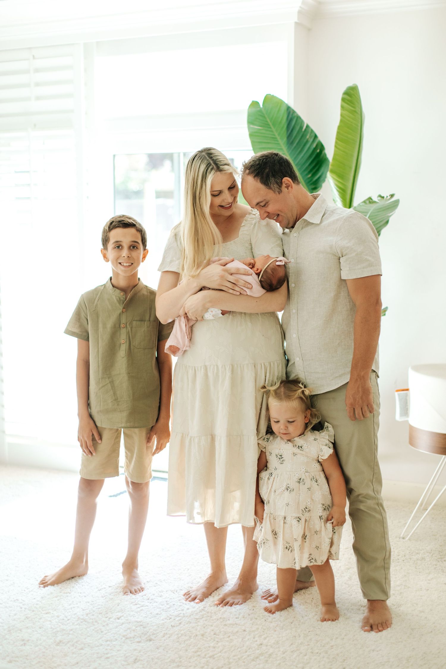 Happy family of five poses together, parents holding newborn and toddler daughter standing with older son.