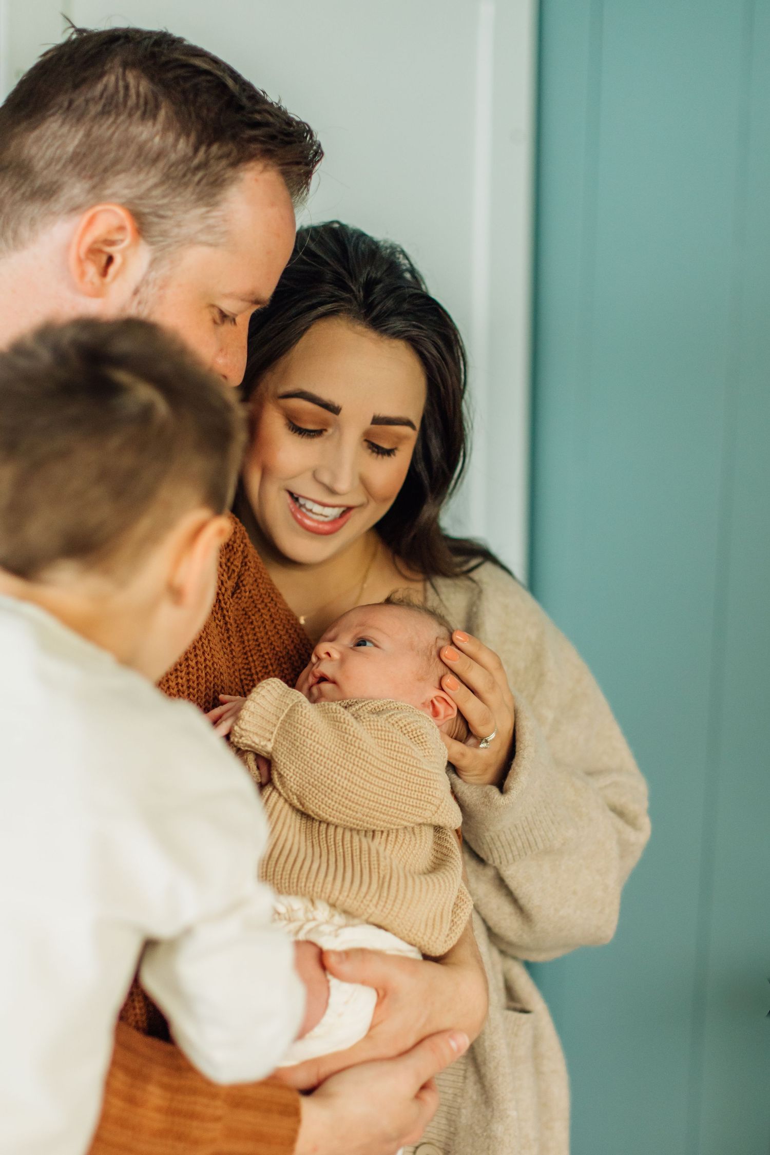 A smiling mother holds her newborn baby as the father kisses her head and their son looks on.