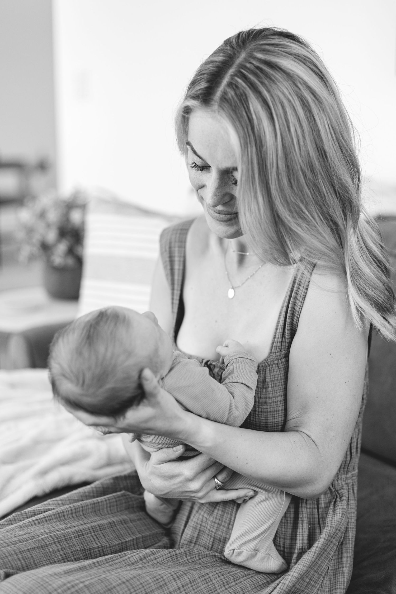 Black and white photo of blonde mother lovingly gazing at her newborn baby indoors.