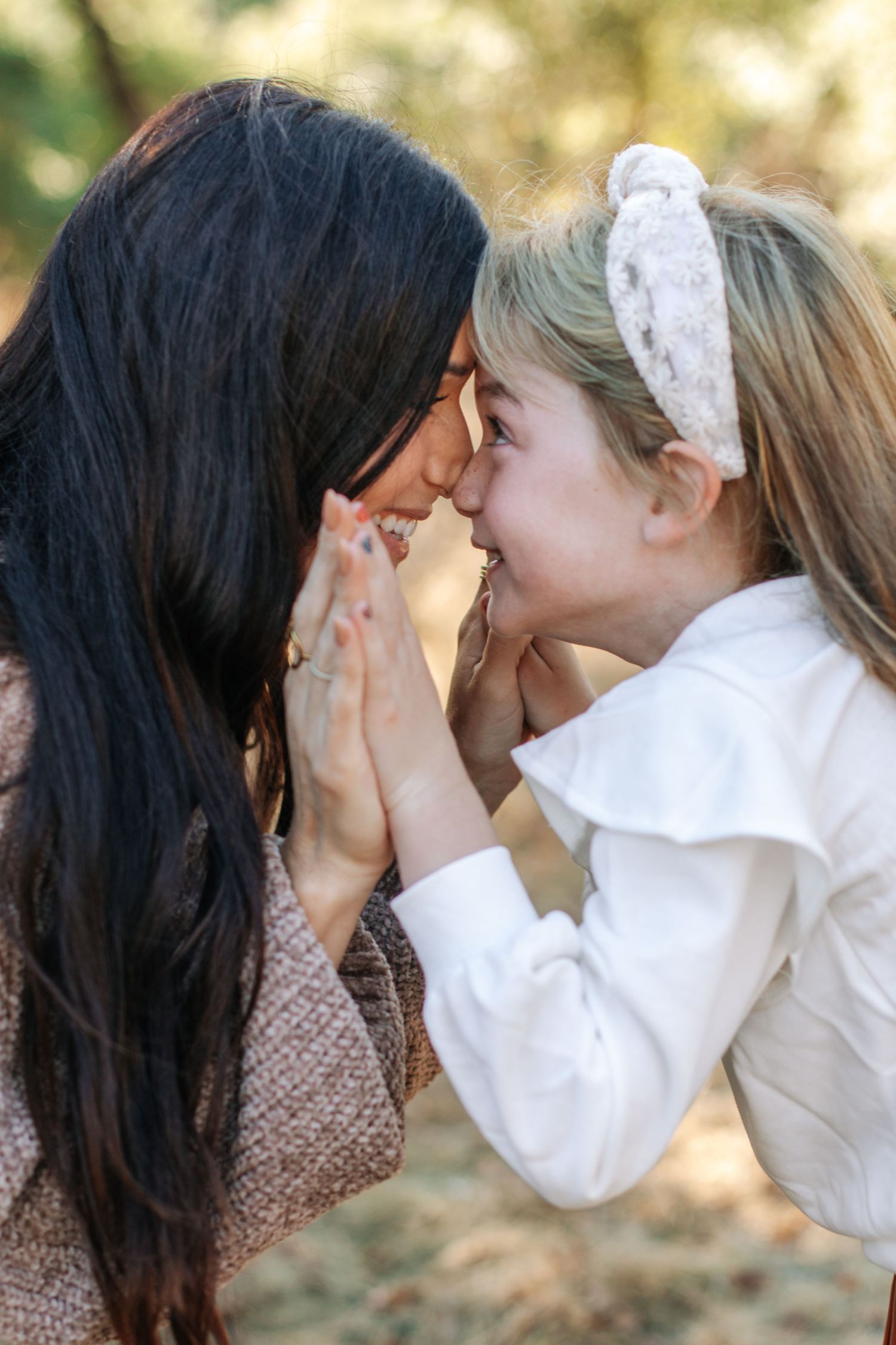 Mother and daughter touching foreheads and smiling warmly in outdoor natural setting.