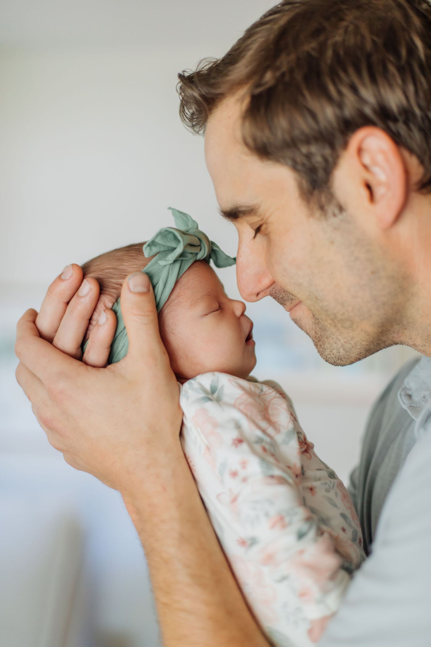 Loving father gently touching noses with his sleeping newborn baby girl in a tender moment.