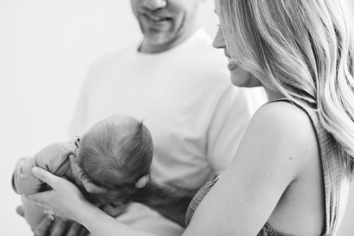 Black and white photo of parents smiling while cradling sleeping newborn baby together.