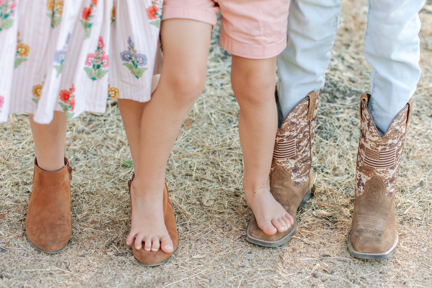 Close-up of three pairs of feet wearing sandals, bare feet, and cowboy boots on dry straw.