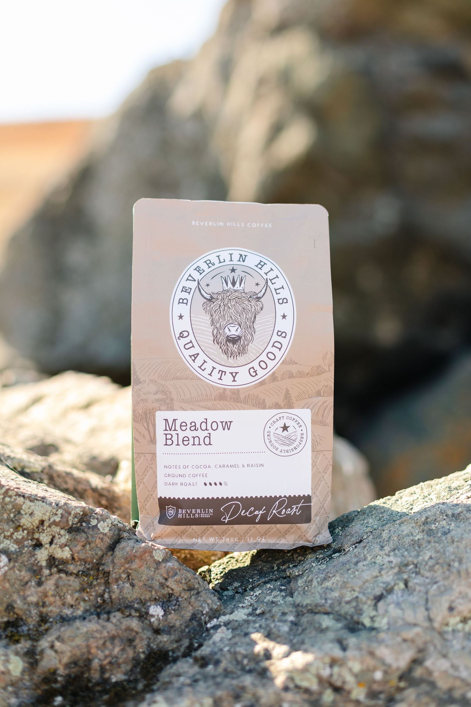 Beverlin Hills Quality Goods Meadow Blend decaf roast coffee bag displayed on rocks outdoors.