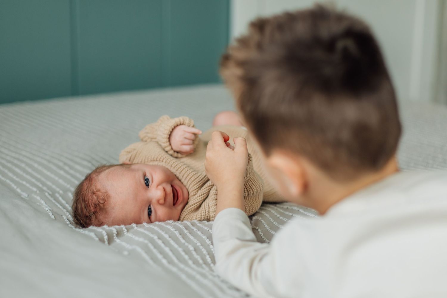 A father leans over his smiling newborn baby lying on a striped bed in a cozy room.