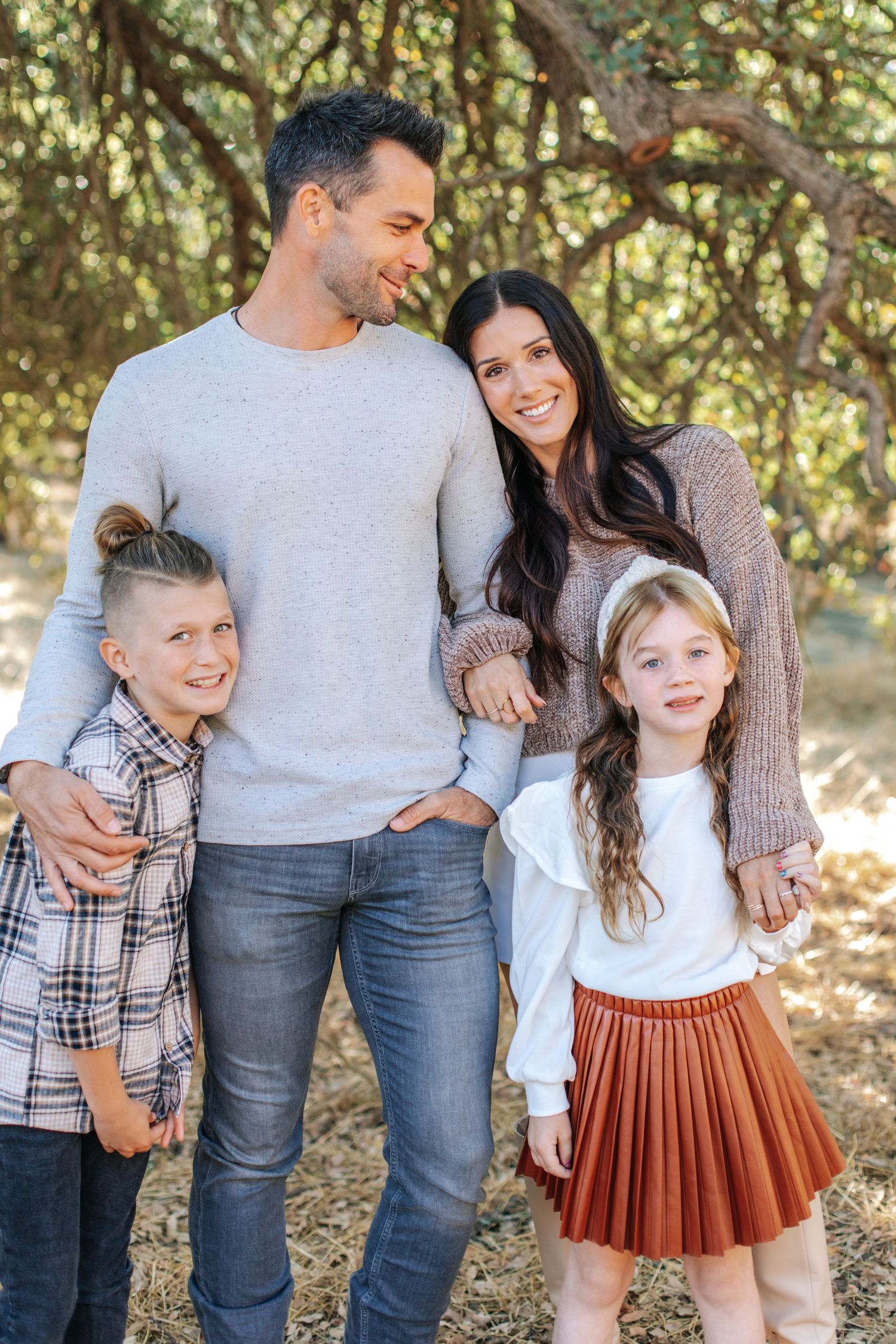Happy family of four posing outdoors among trees in coordinated fall outfits.