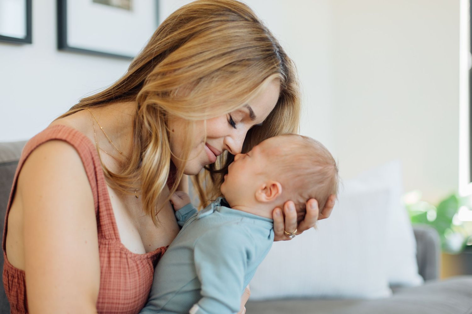 Loving mother smiling and cuddling her newborn baby indoors in natural light.