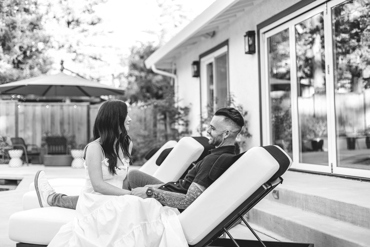 Couple relaxing together on patio chairs in a black and white outdoor portrait photo.