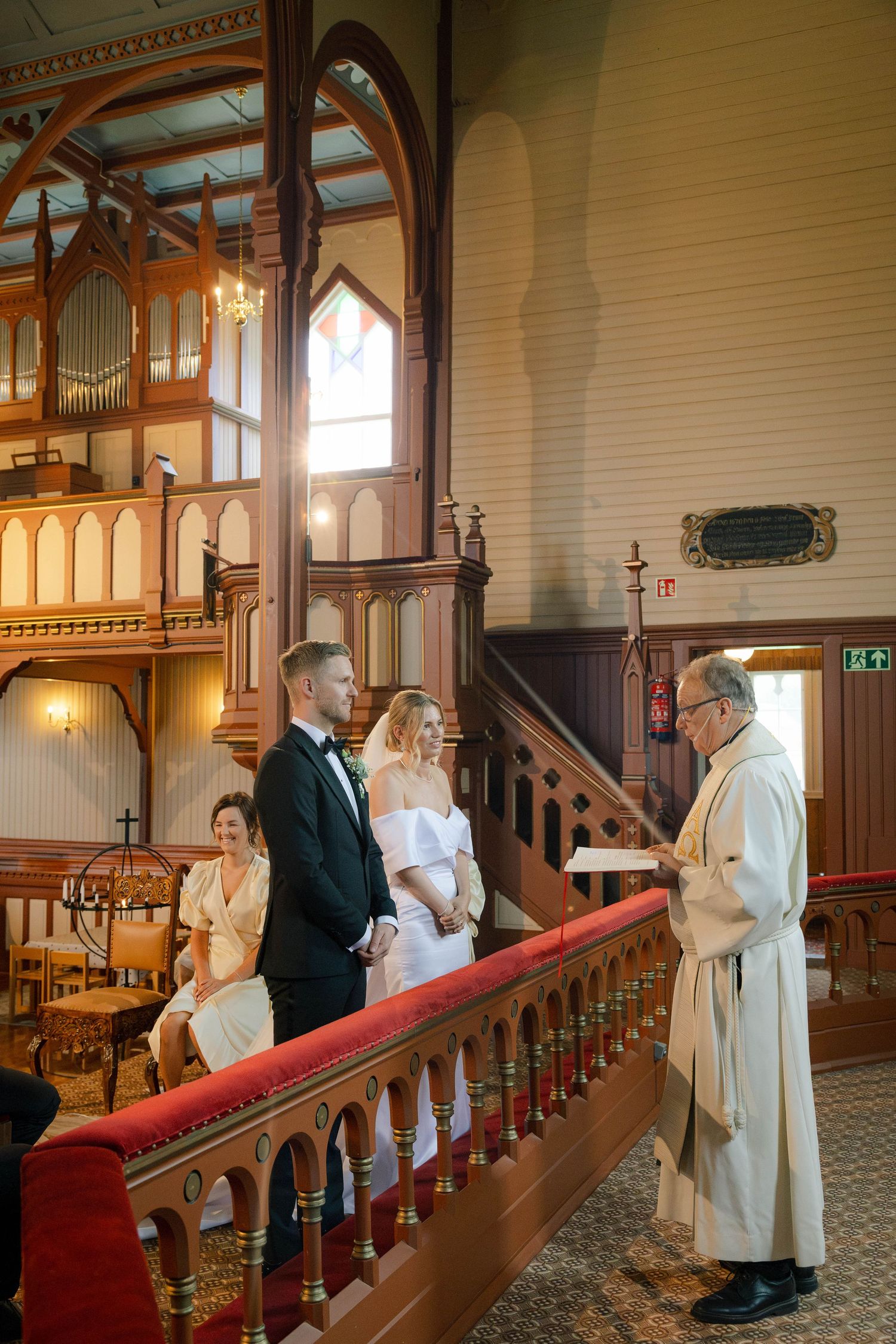 Bride and groom stand at altar during church wedding ceremony with officiant in white robe.