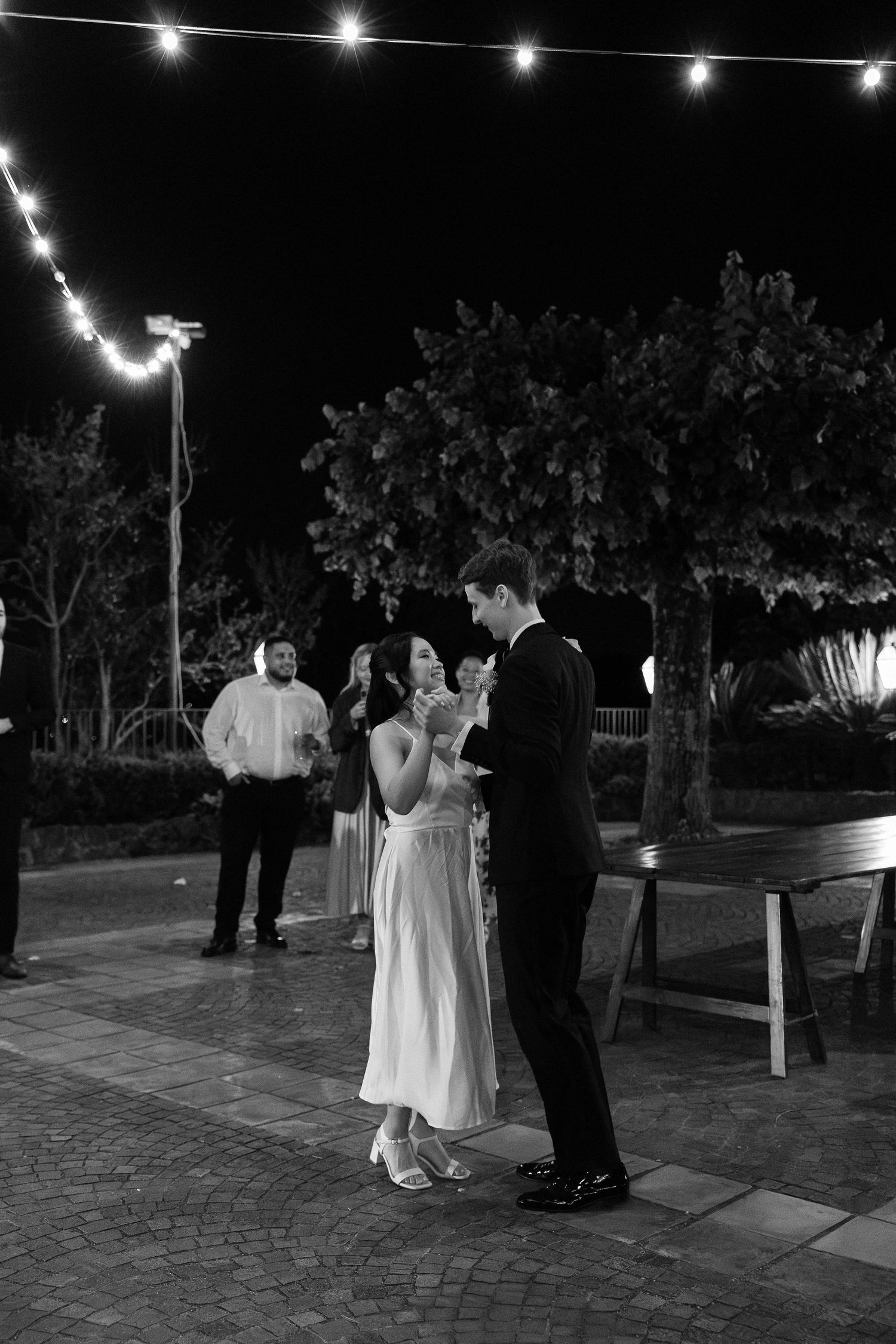 Black and white photo of bride and groom sharing first dance at outdoor evening wedding reception.