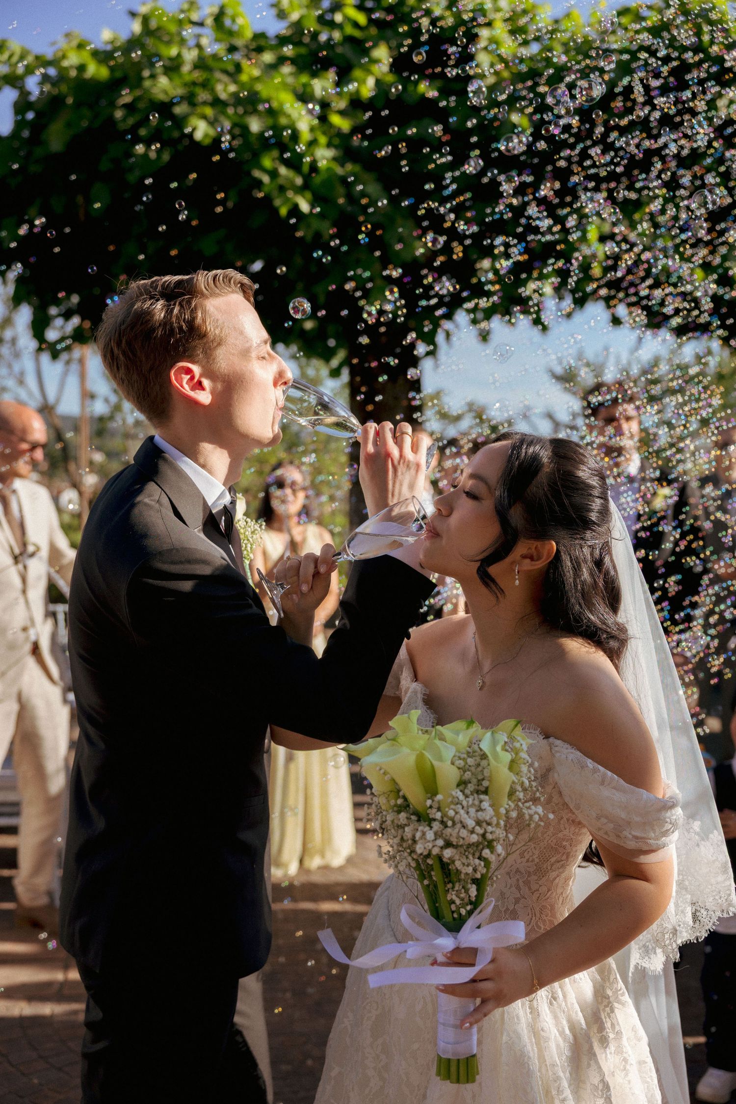 Bride and groom blowing bubbles together outdoors during wedding ceremony exit celebration.