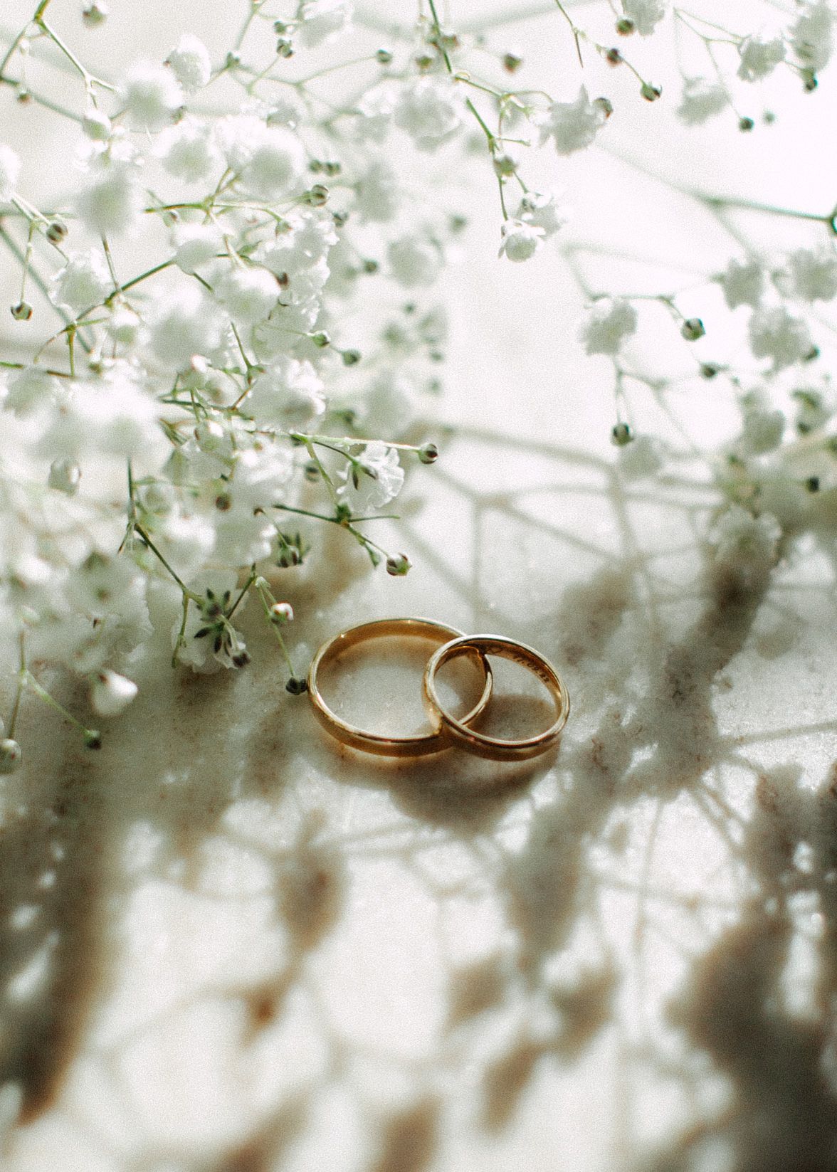Two gold wedding rings resting among delicate white baby's breath flowers on a soft light background.
